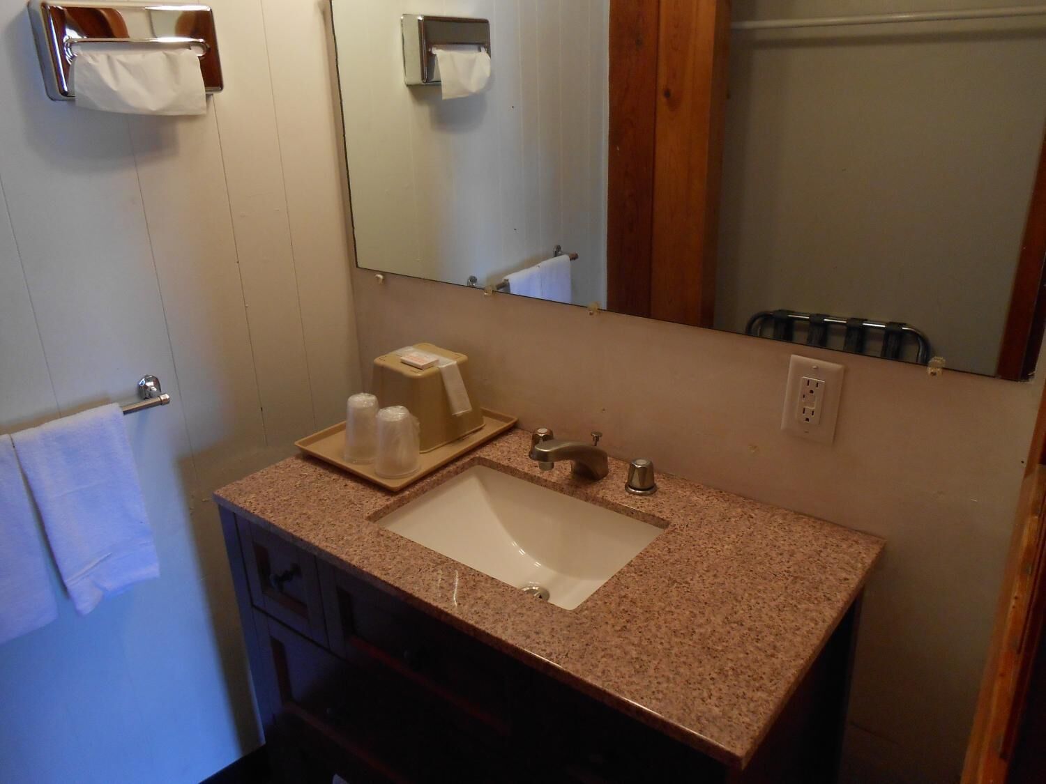 A bathroom with a granite countertop sink, a mirror, a towel rack, and a soap dispenser.