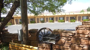 A stone wall with a grill and a bench in a parking lot area. - Redrock Country Inn (Kanab)