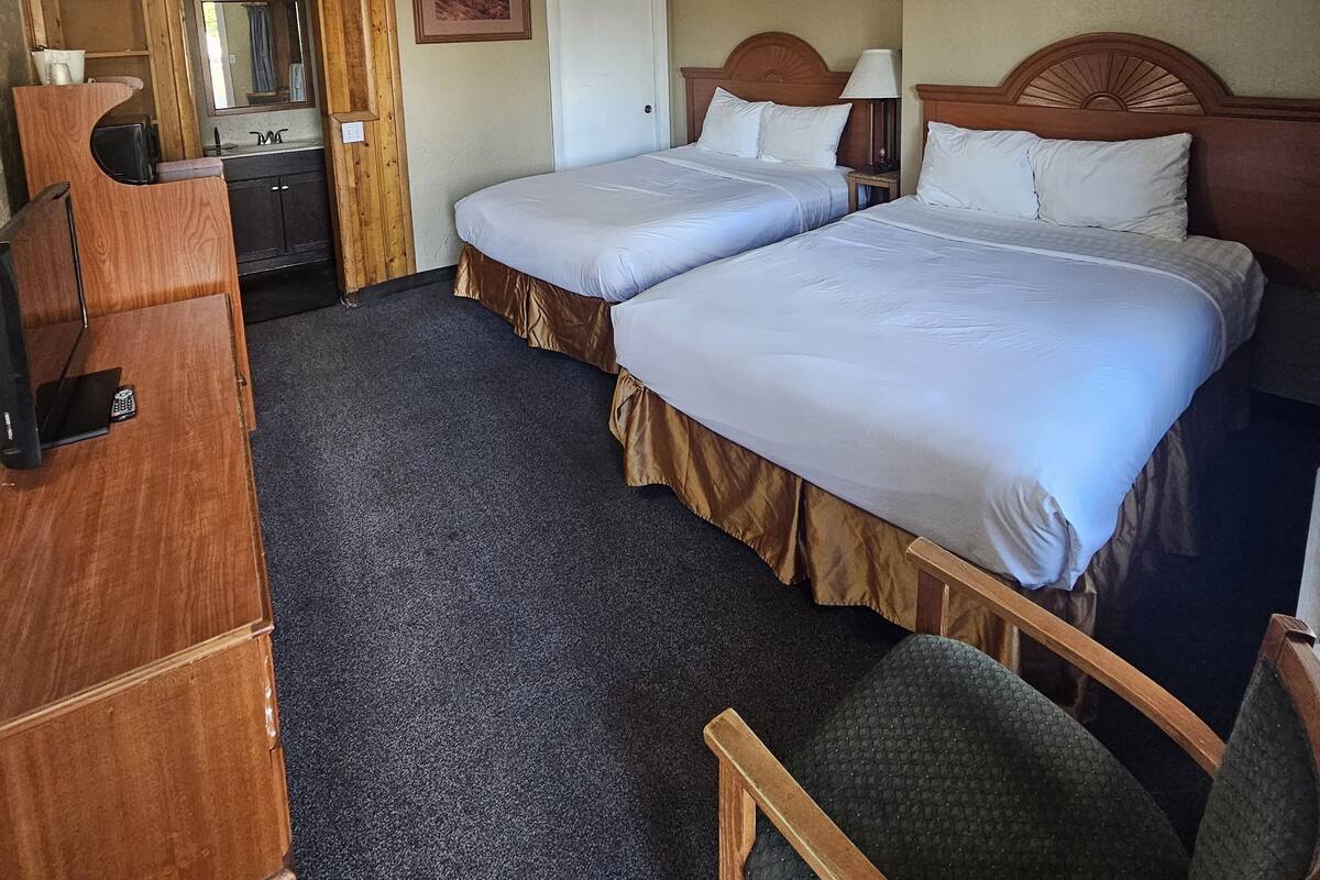 A hotel room with two beds, a desk, a chair, a dresser, and a mirror.