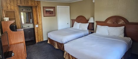 A hotel room with two beds, a desk, a chair, a dresser, and a mirror.