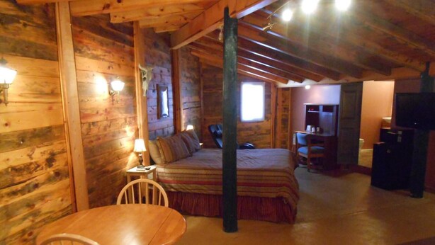 A cozy log cabin room with a bed, a dining table with chairs, and a television. - Redrock Country Inn (Kanab)