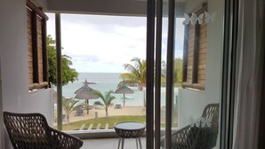 Un balcón con sillas de mimbre, una mesita redonda y vista al océano y la playa, con sombrillas.