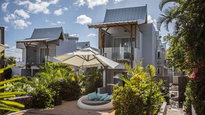 Una villa moderna con un área de estar cubierta al aire libre, rodeada de exuberante vegetación y un cielo despejado.