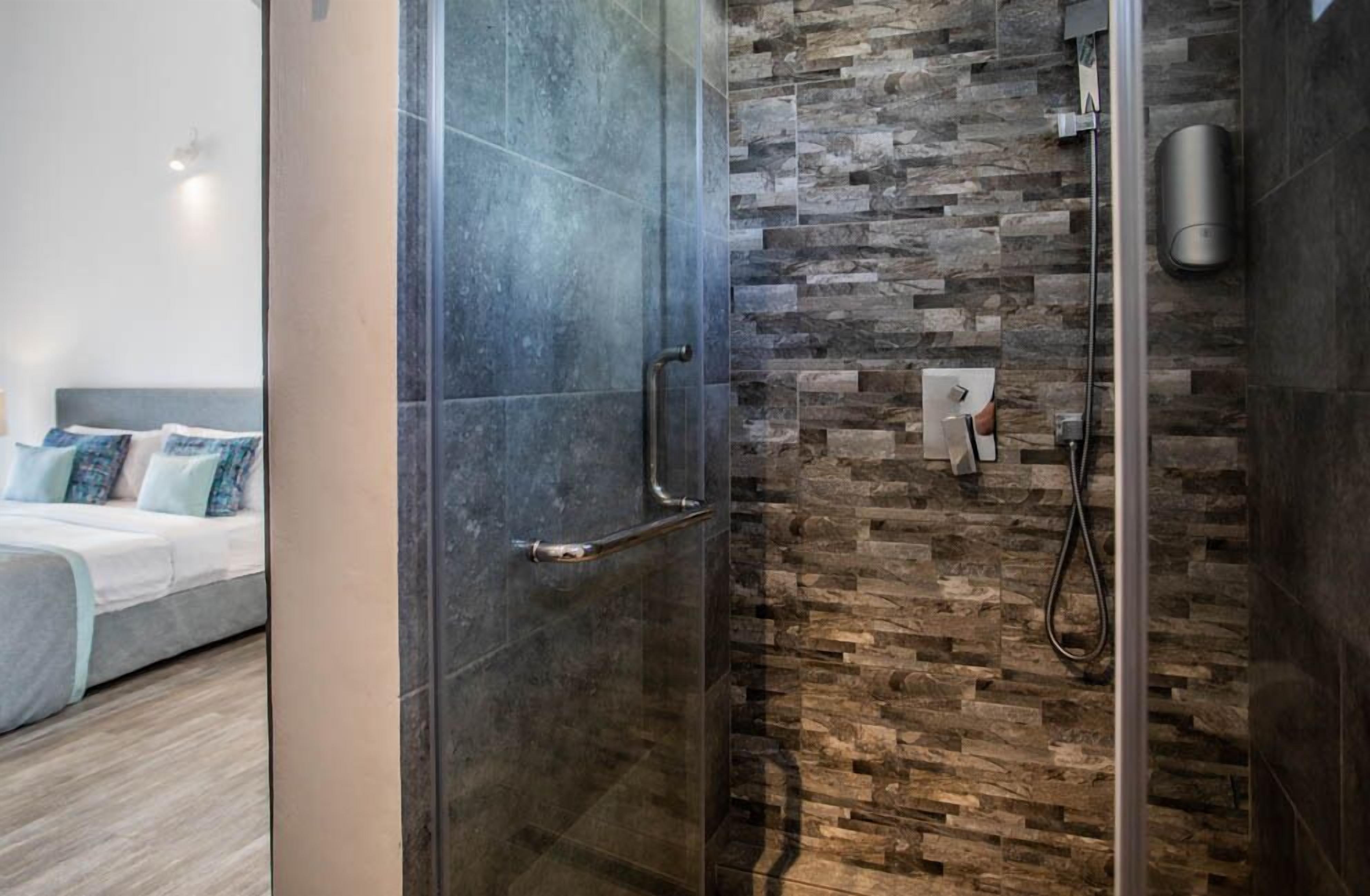 A modern bathroom with a glass shower enclosure, a stone mosaic wall, and a visible control panel.