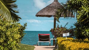 Un área de descanso en la playa con una sombrilla de paja, un banco y un cartel que indica los horarios del atardecer.