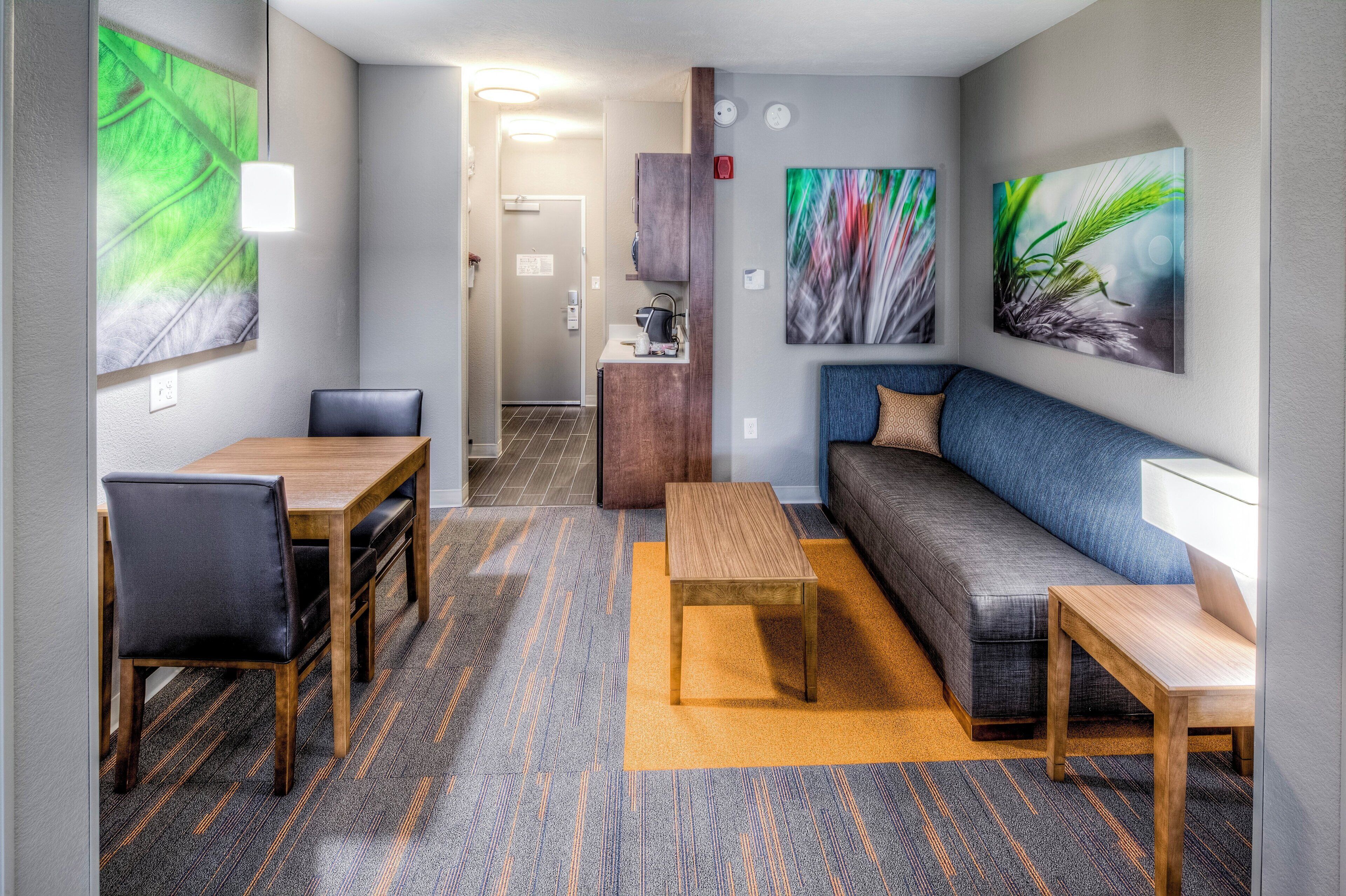 Habitació d'hotel amb zona de menjador, sofà, taula de cafè i obres d'art a les parets.