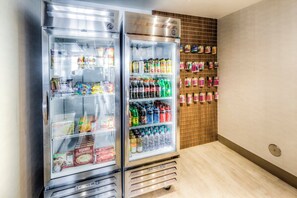 Two beverage-air coolers stocked with snacks, drinks, and condiments in a room with wooden paneling and tiled flooring. - Holiday Inn Express & Suites Cleveland West - Westlake by IHG (Westlake)