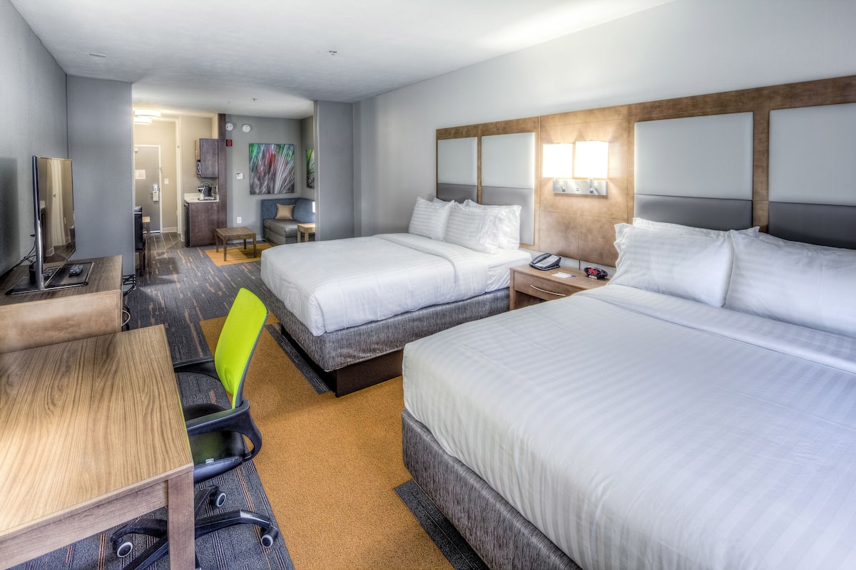A hotel room with two single beds, a desk, a chair, a small table, a sofa, and a kitchenette.