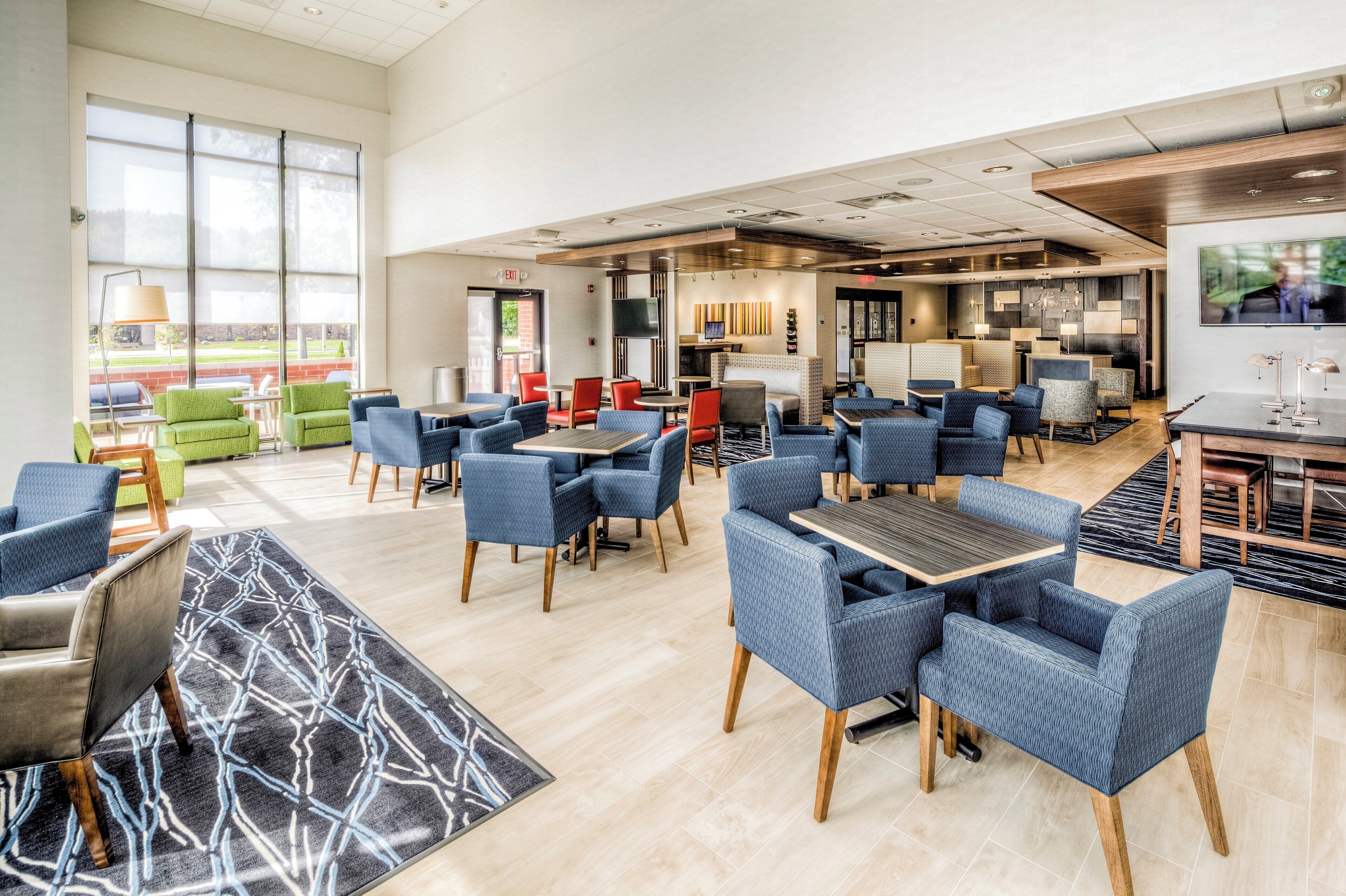 A spacious indoor area with multiple seating arrangements, including tables and chairs, and a large window providing natural light.