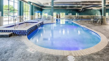Una piscina interior con borde de azulejos azules, sillas de descanso y zona de sol.