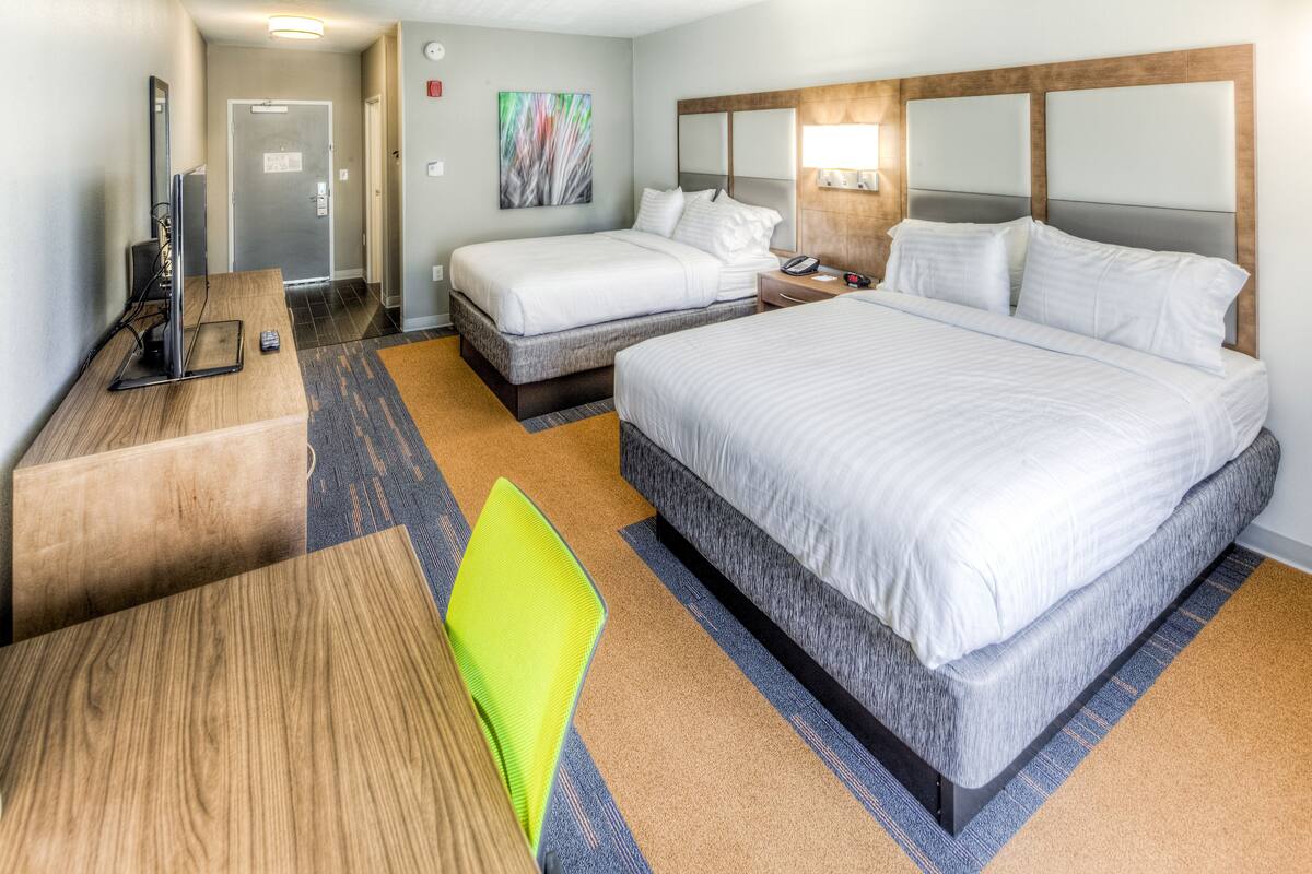 A hotel room with a large bed, a smaller bed, a desk with a computer, and a chair.