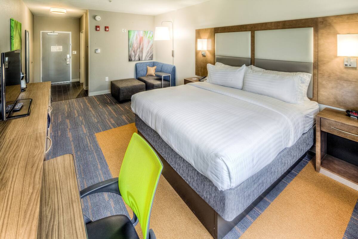 A hotel room with a large bed, a desk, a chair, a TV, and a bathroom door.