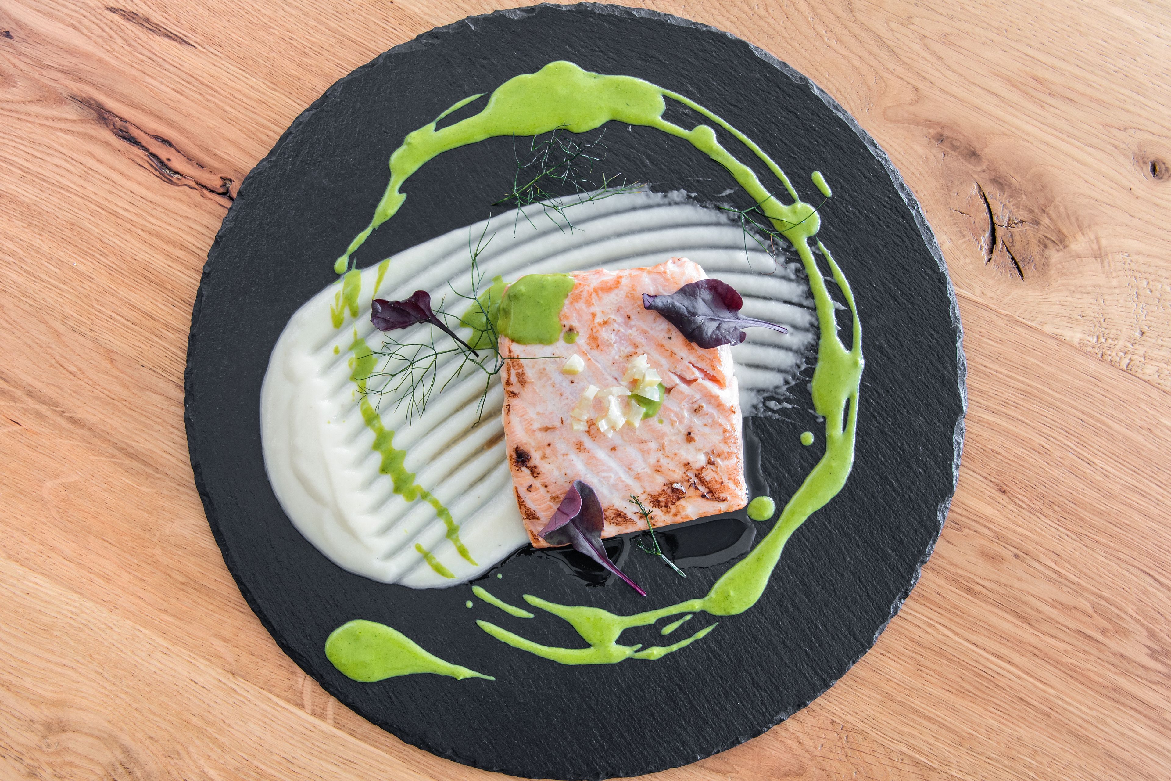 Un plato de salmón con salsa verde y vegetales sobre un plato negro.