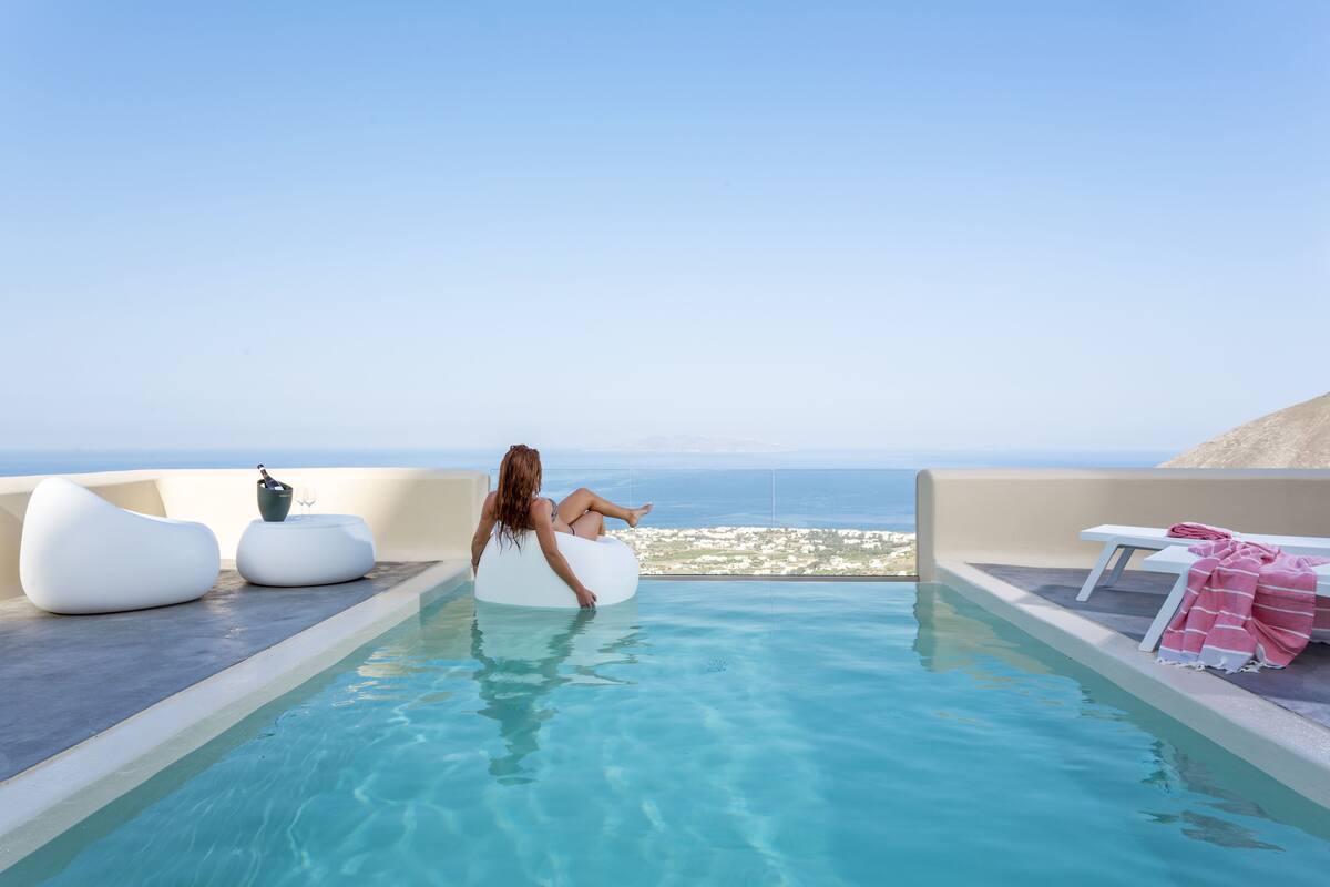 Zona de piscina con vista al mar, sillas de descanso blancas y una botella de champán.