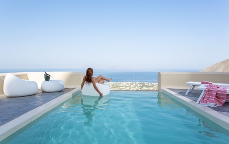 A pool area with a view of the sea, white lounge chairs, and a bottle of champagne.