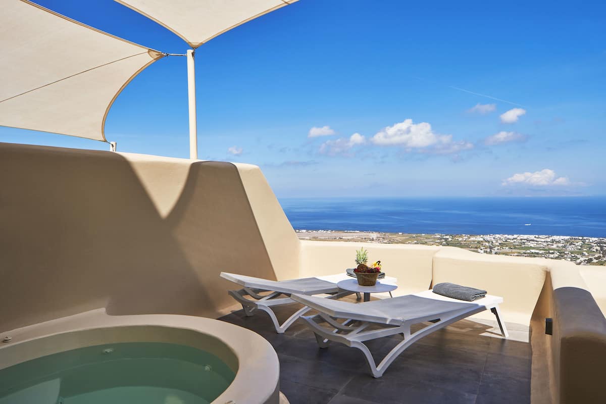 Un balcón con un jacuzzi, dos sillones de descanso, una mesita con una planta y vistas al mar y al pueblo.