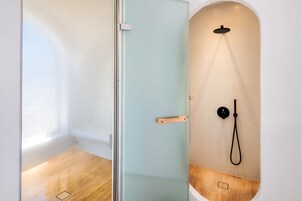 A modern bathroom with a glass shower enclosure, a wooden floor, and a tiled wall.