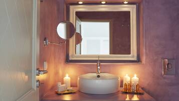 A bathroom with a round sink, a mirror, and three lit candles on the counter.