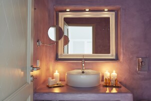 A bathroom with a round sink, a mirror, and three lit candles on the counter.