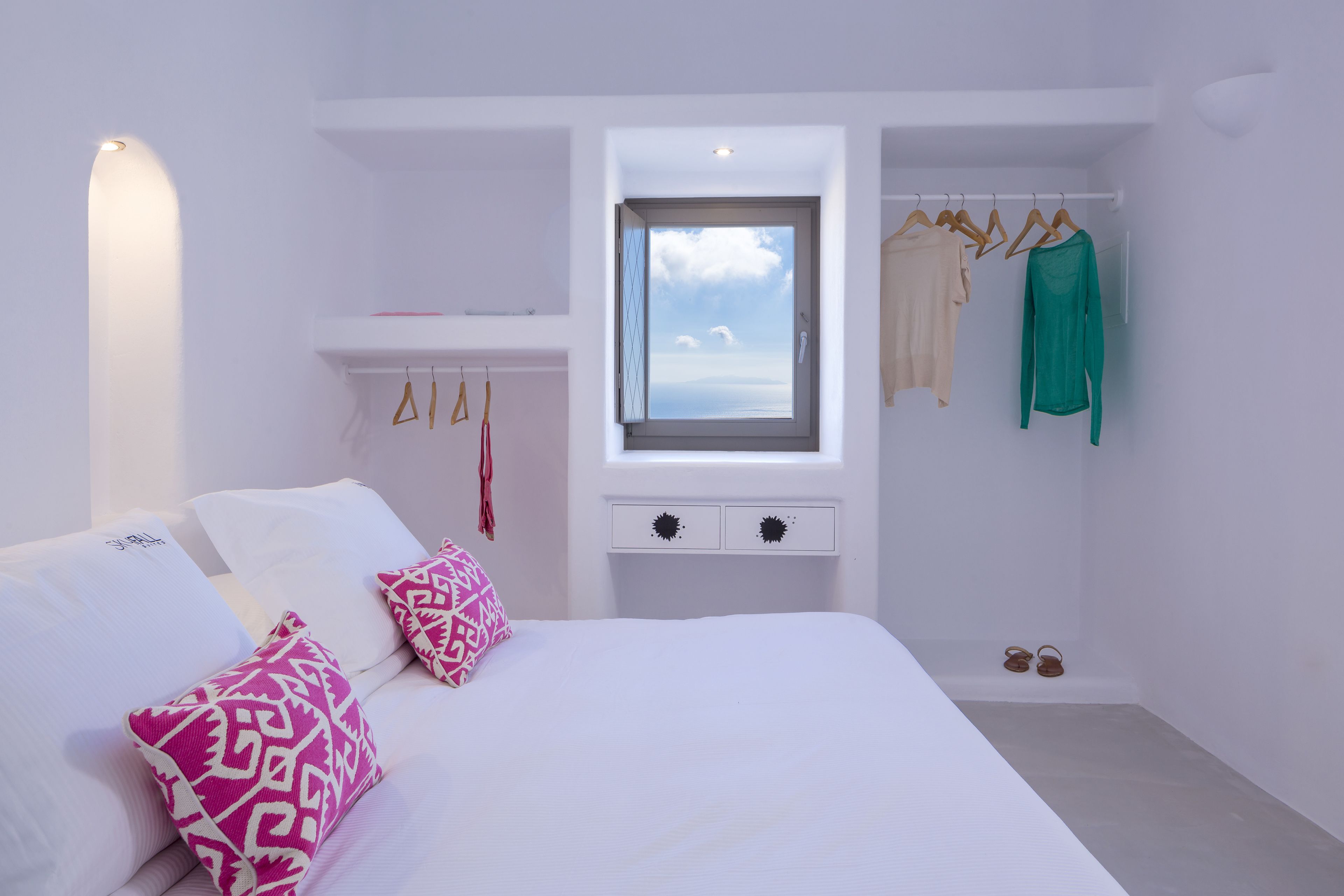 A bedroom with a bed, pillows, a window, a wardrobe, and a small table.