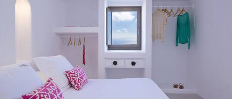 A bedroom with a bed, pillows, a window, a wardrobe, and a small table.