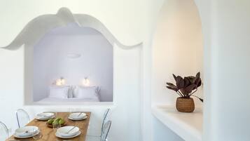 A dining area with a wooden table set for two, clear glass chairs, and a white arched ceiling.