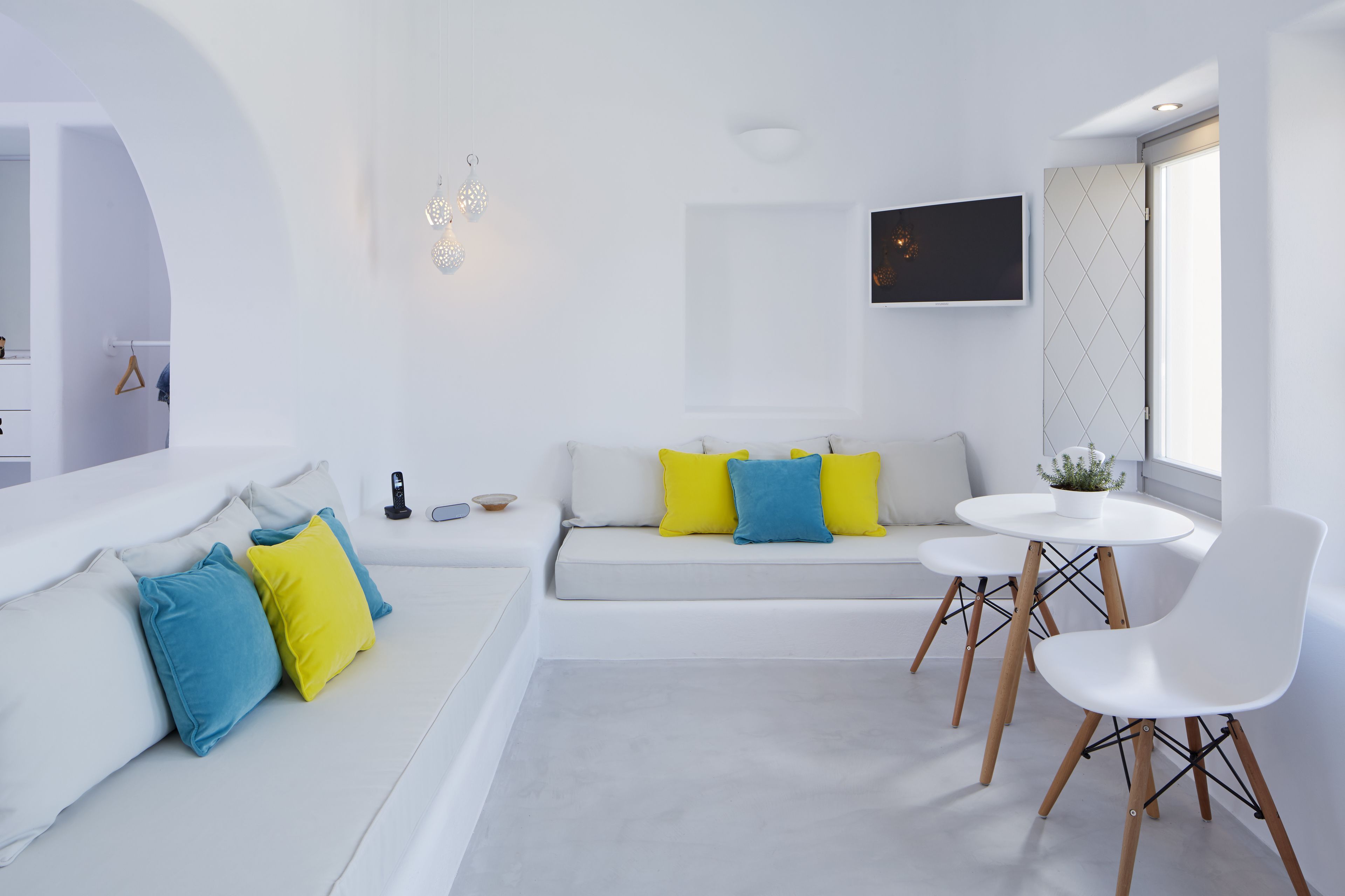 A modern, minimalist living room with a white sofa, a round table, and two white chairs.