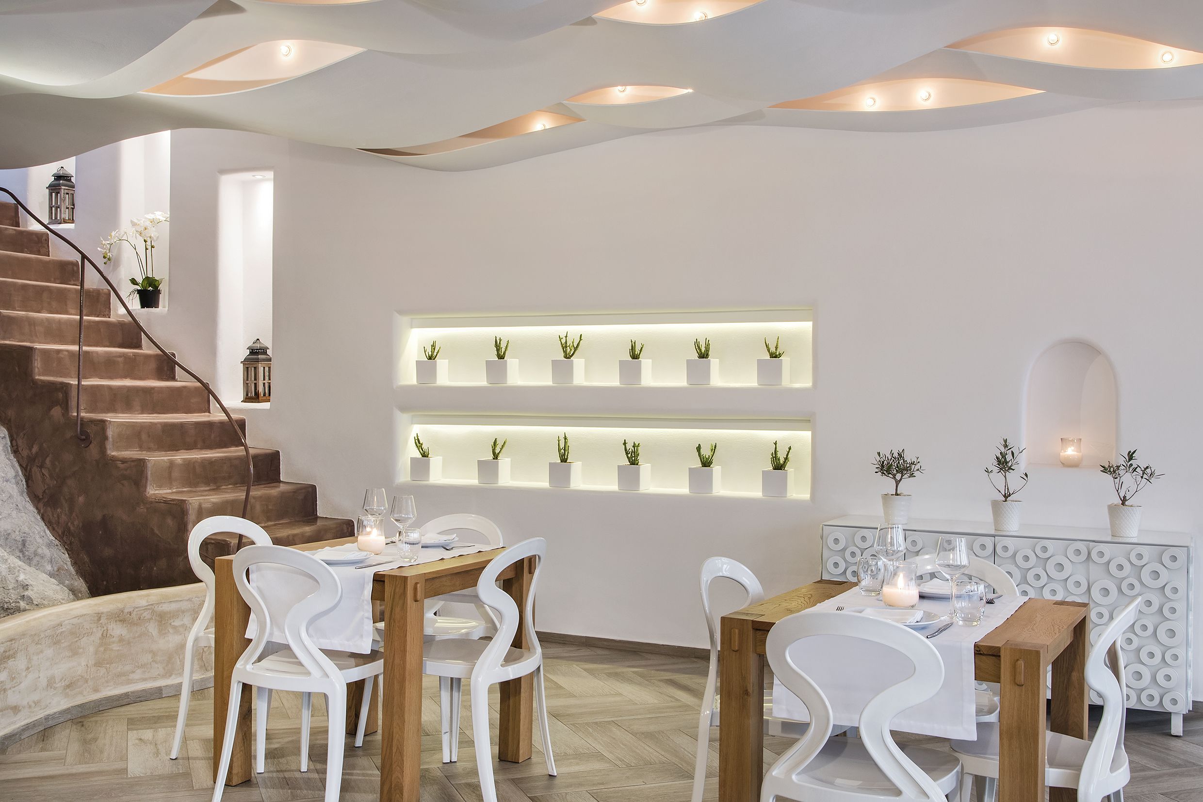 Een modern interieur met een trap, witte meubels en planten in potten op planken.