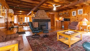 A cozy log cabin interior with a fireplace, leather chairs, a dining area, and a kitchen.