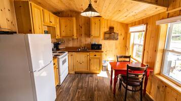 Een houten chalet van binnen, met een keuken, een eethoek en grote ramen.
