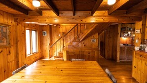 A wooden cabin interior with a dining area, staircase, and kitchen.