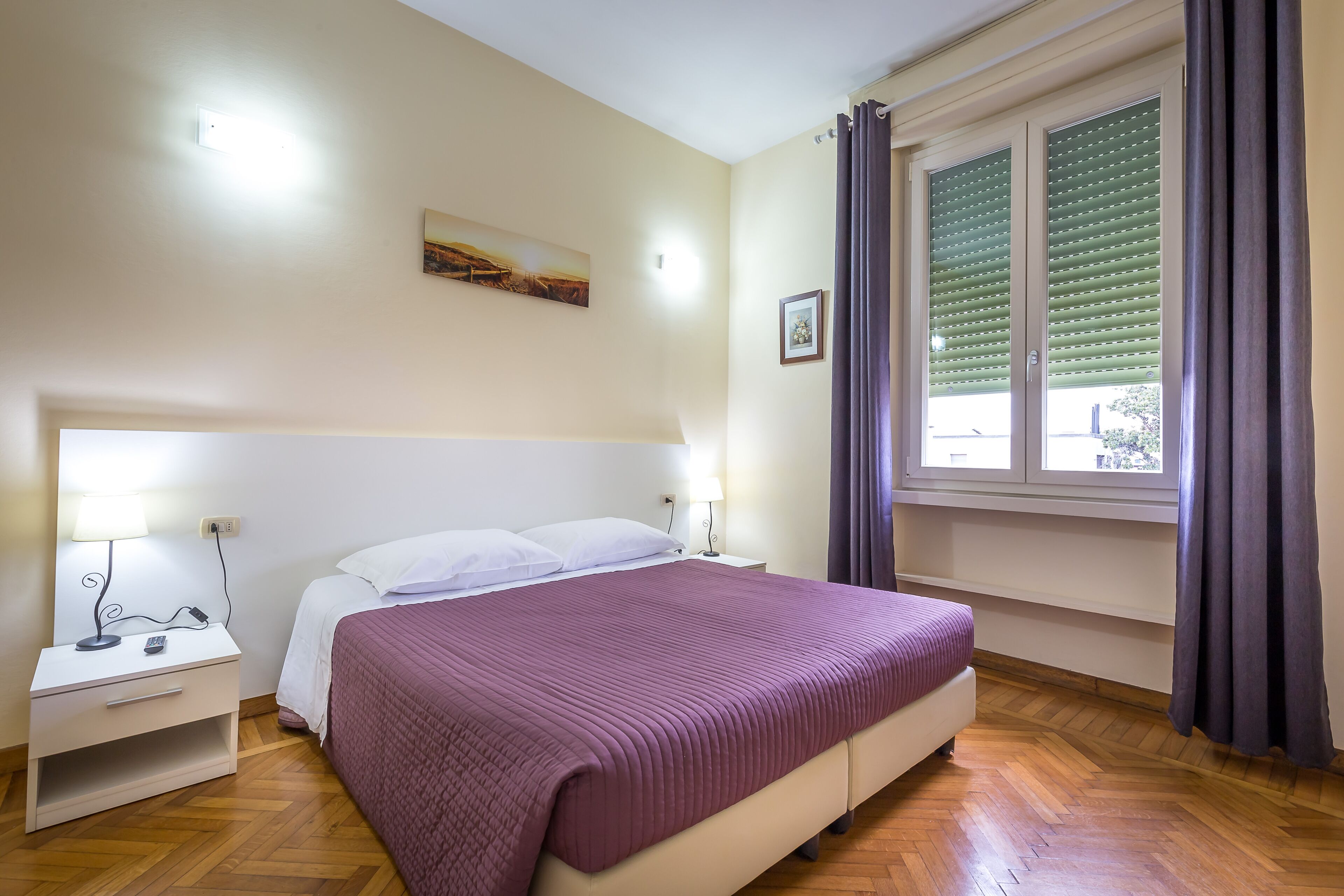A bedroom with a bed, bedside table, lamp, and window with curtains.