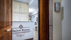 En hotellobby med en skylt som visar texten ”Maison Bianca”, en trädörr och en väggmonterad intercom.