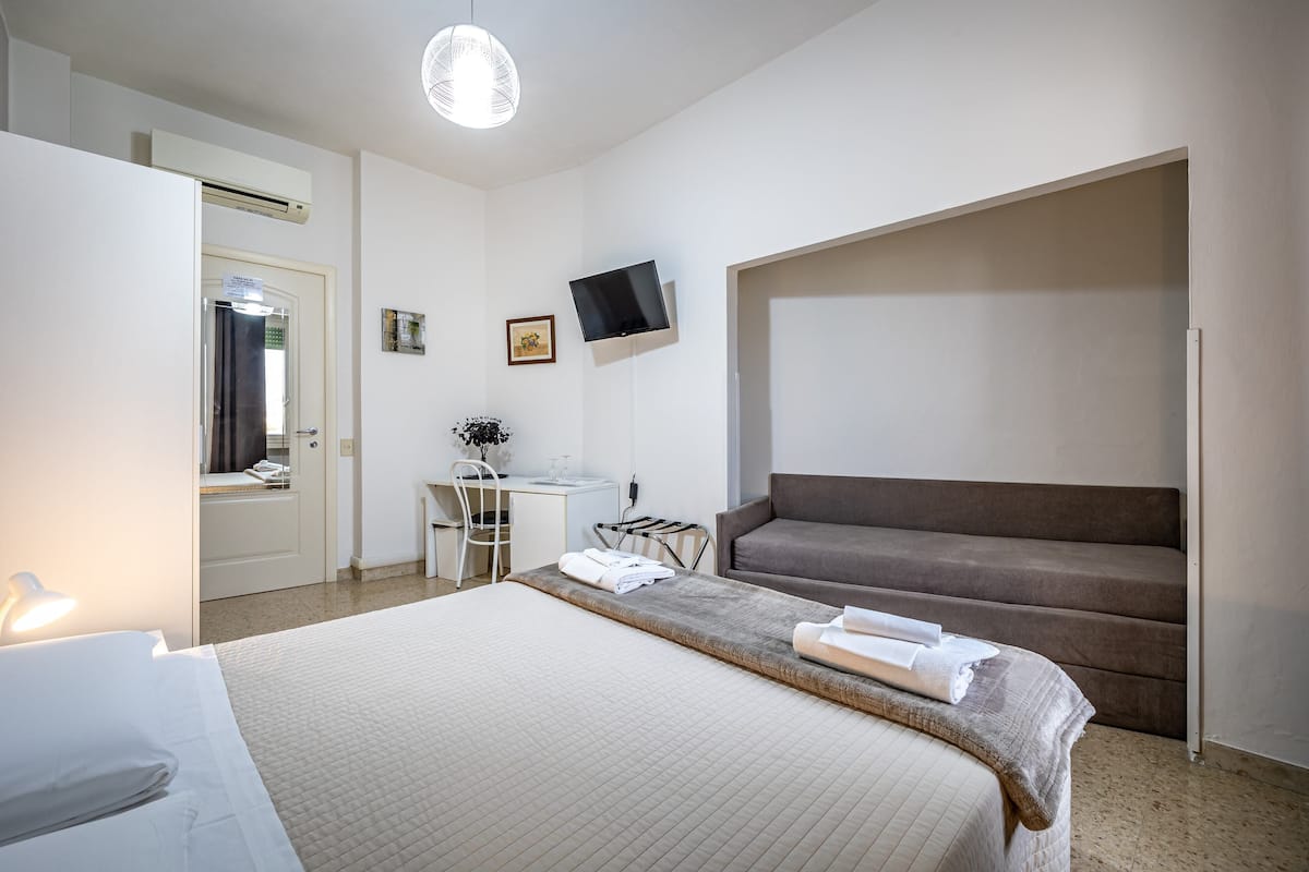 A hotel room with a bed, a desk, a chair, a TV, and a sofa.