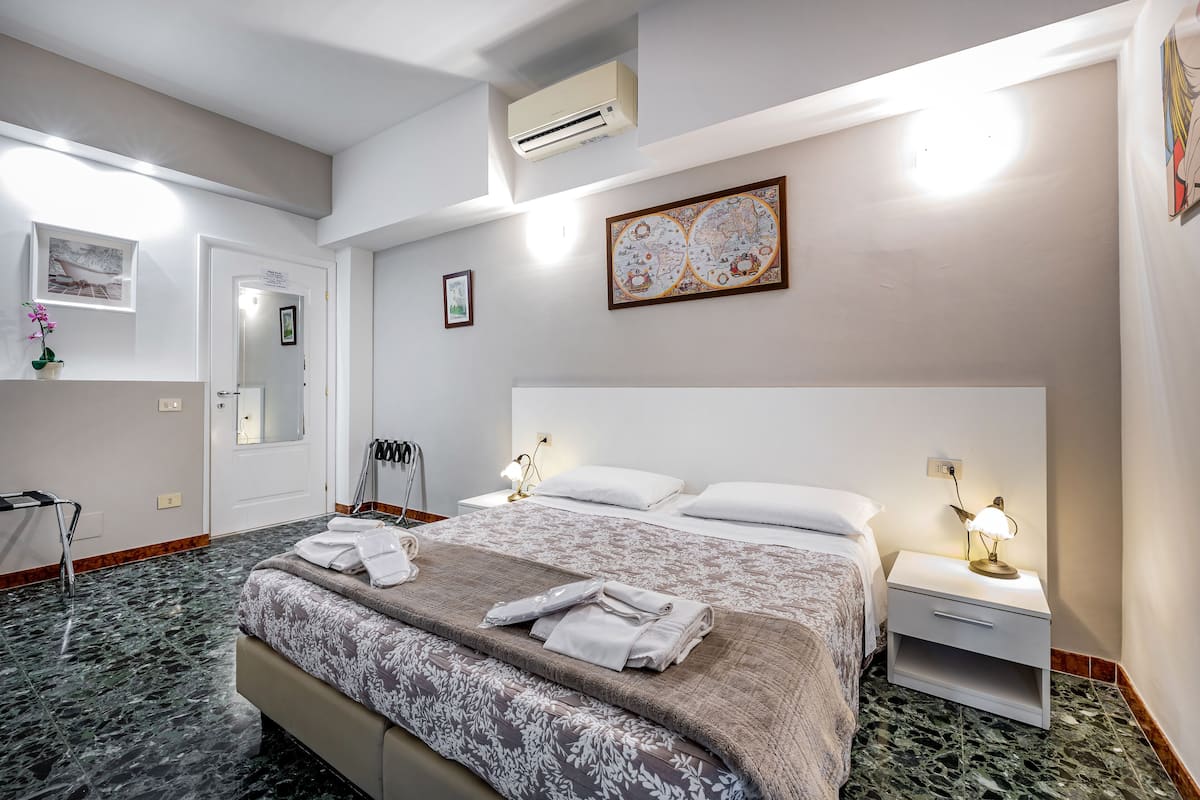 A hotel room with a large bed, two bedside tables with lamps, a wall-mounted air conditioner, and a framed map on the wall.