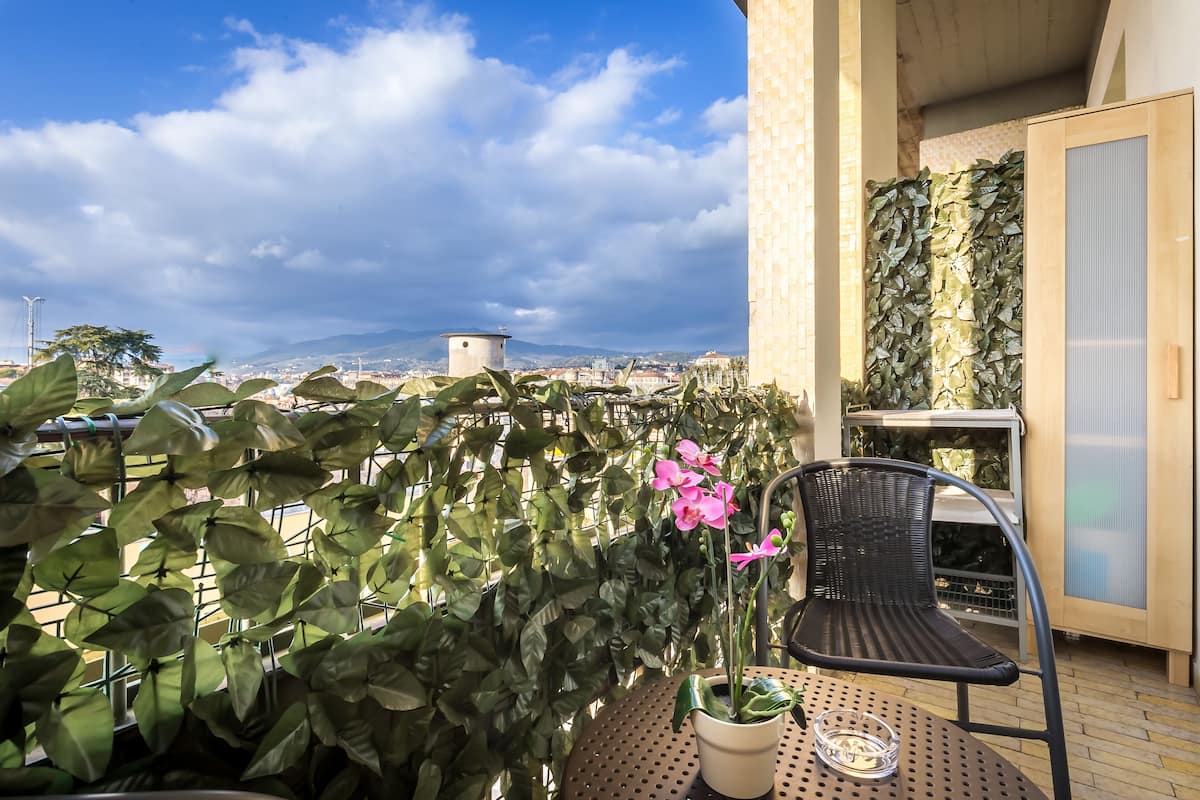A balcony with a potted plant, a chair, and a view of a cityscape.