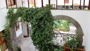 Un atrio de varios niveles con una escalera central, paredes de piedra y plantas en macetas.