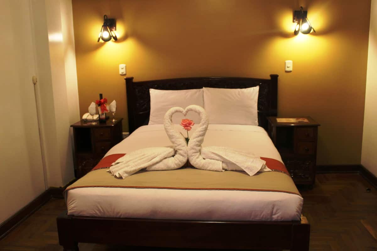 A hotel room with a bed, two nightstands, and wall-mounted lamps.