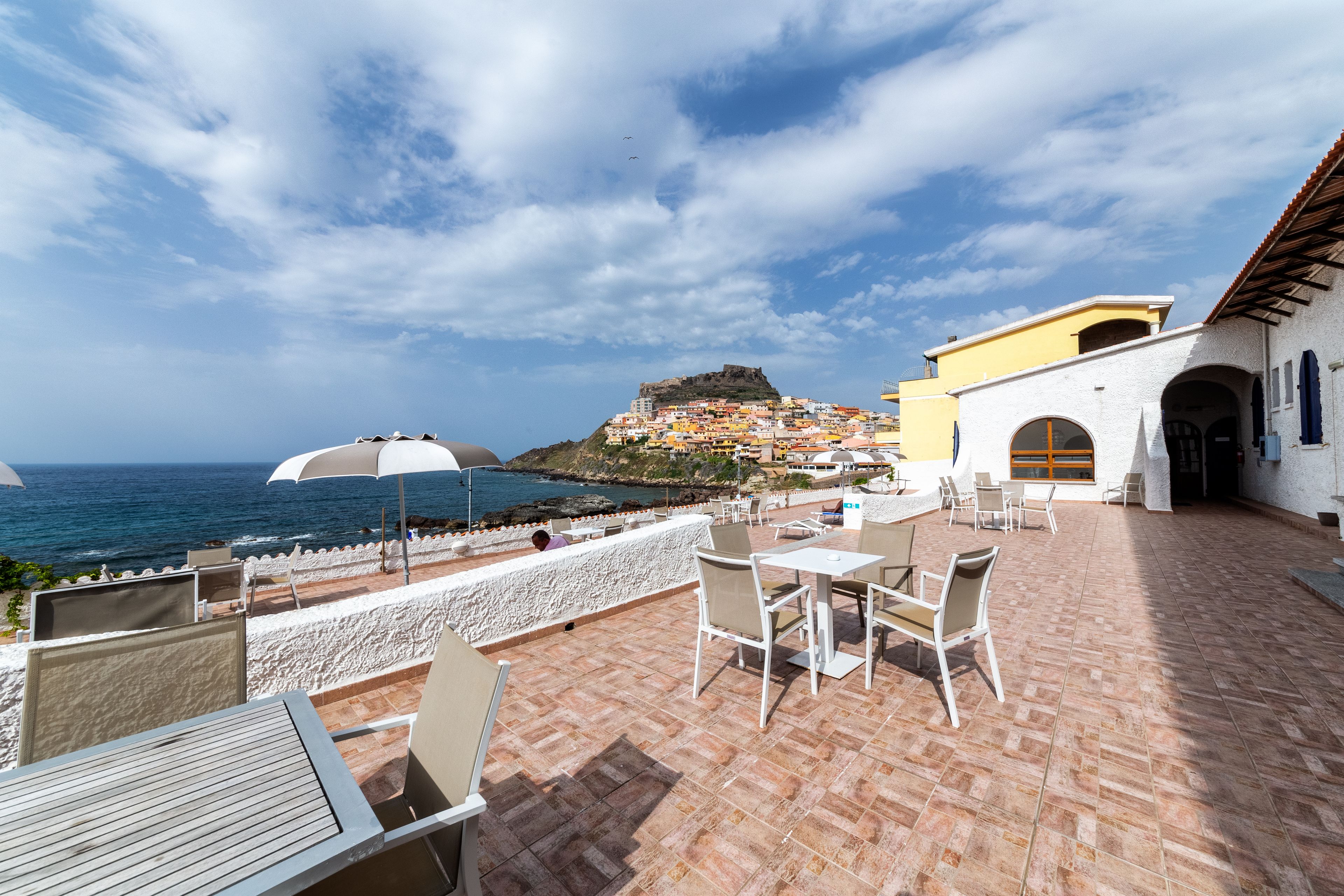 Una terraza con asientos al aire libre, vista al mar y una colina con edificios al fondo.