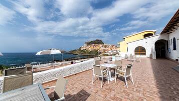 Una terraza con asientos al aire libre, vista al mar y una colina con edificios al fondo.