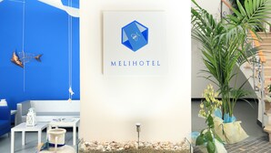 Un vestíbulo de hotel moderno con una pared azul de acento, un logotipo enmarcado y diversas plantas.