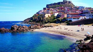 Un pueblo costero con edificios coloridos, una playa y una colina destacada con una fortificación.