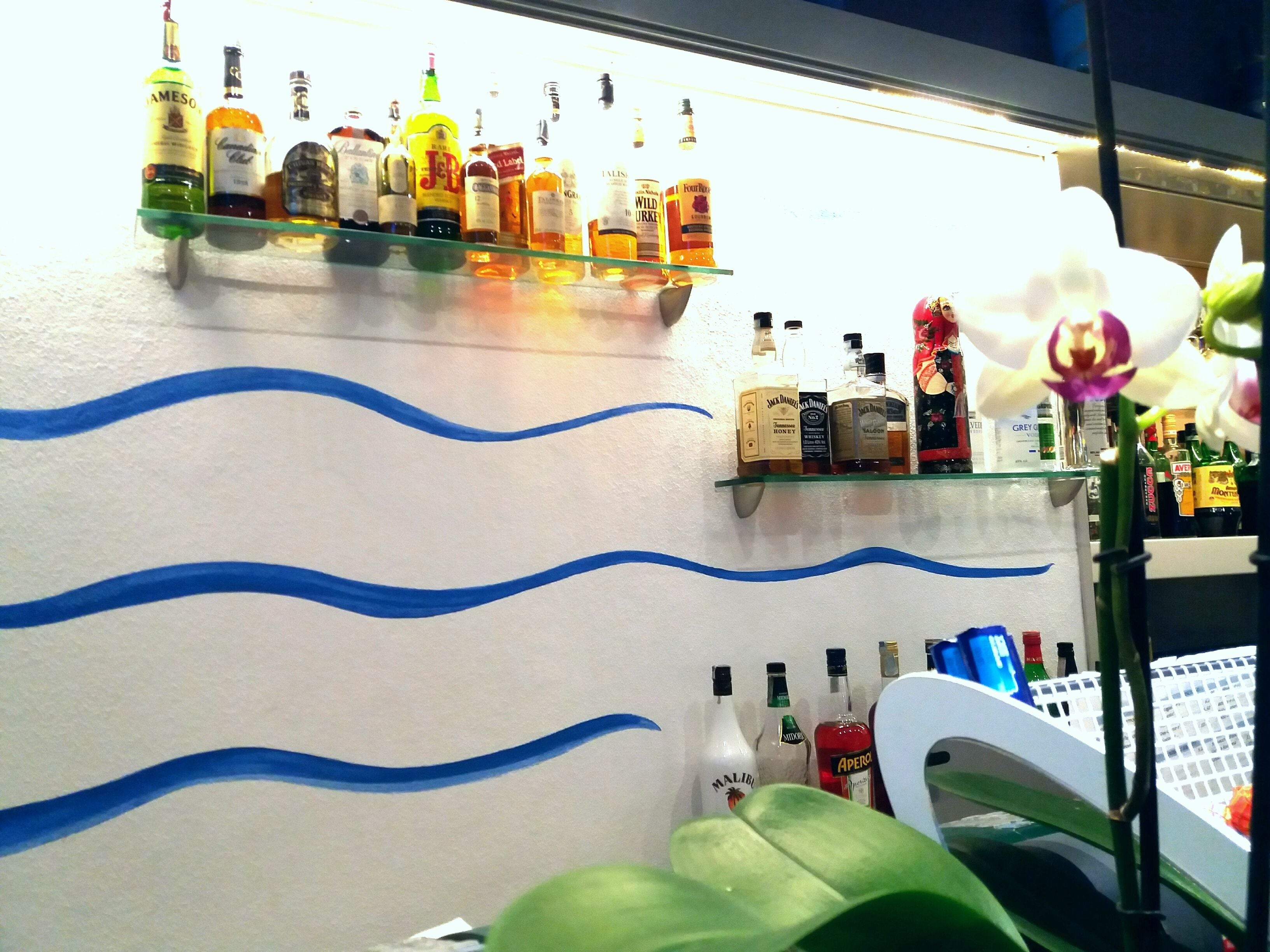 A bar area with shelves of liquor bottles and a decorative wall with blue wavy lines.
