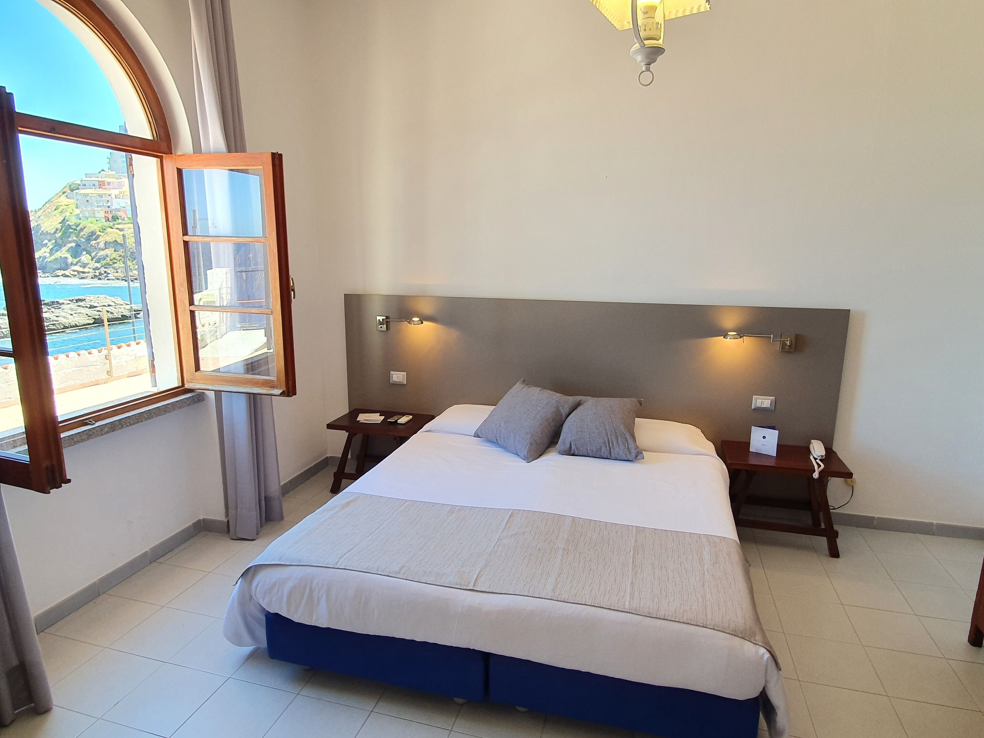Une chambre à coucher comprenant un lit, des tables de chevet, une commode, une lampe et une fenêtre donnant sur un paysage côtier.