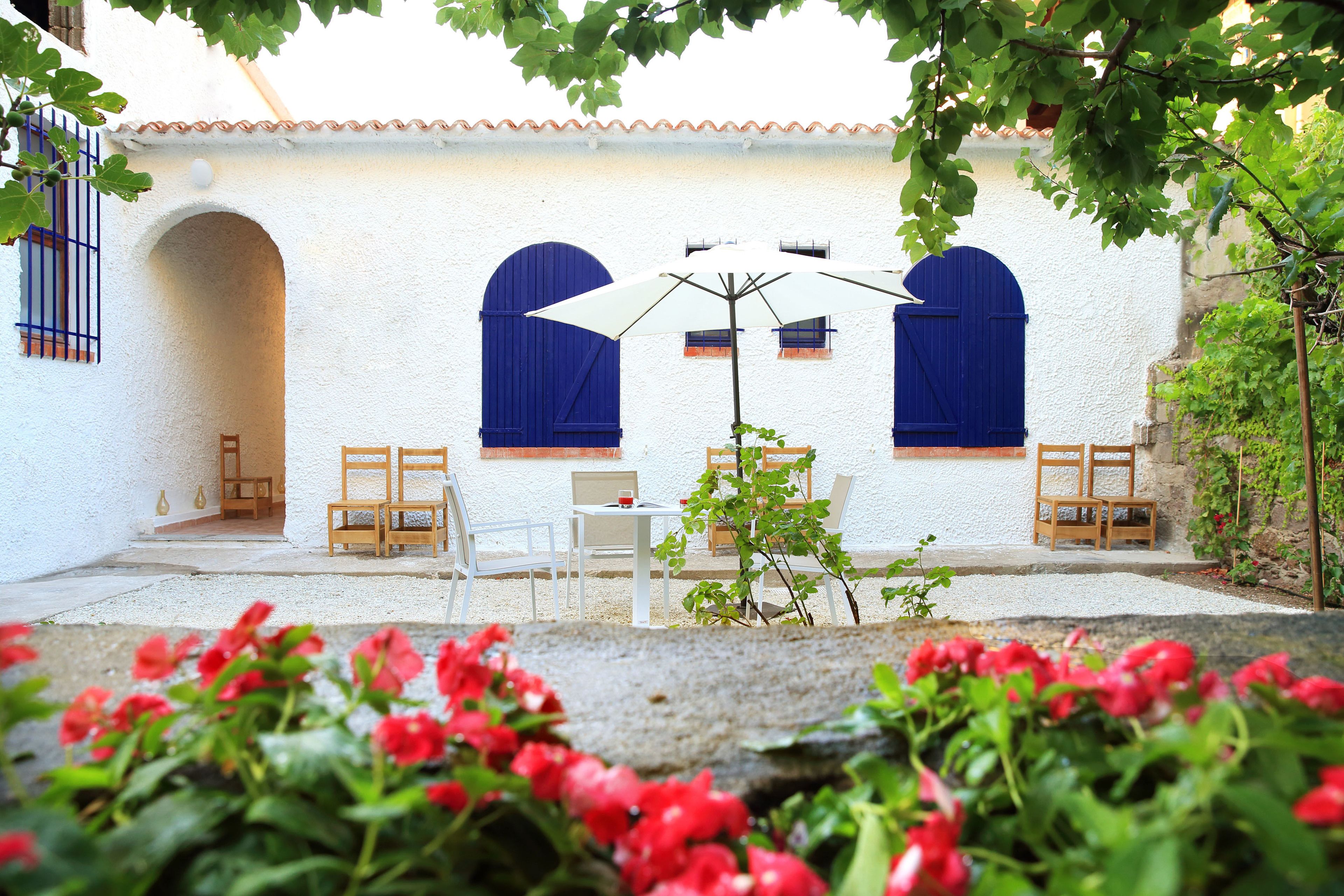 A courtyard with white walls, blue shutters, and a table with chairs.