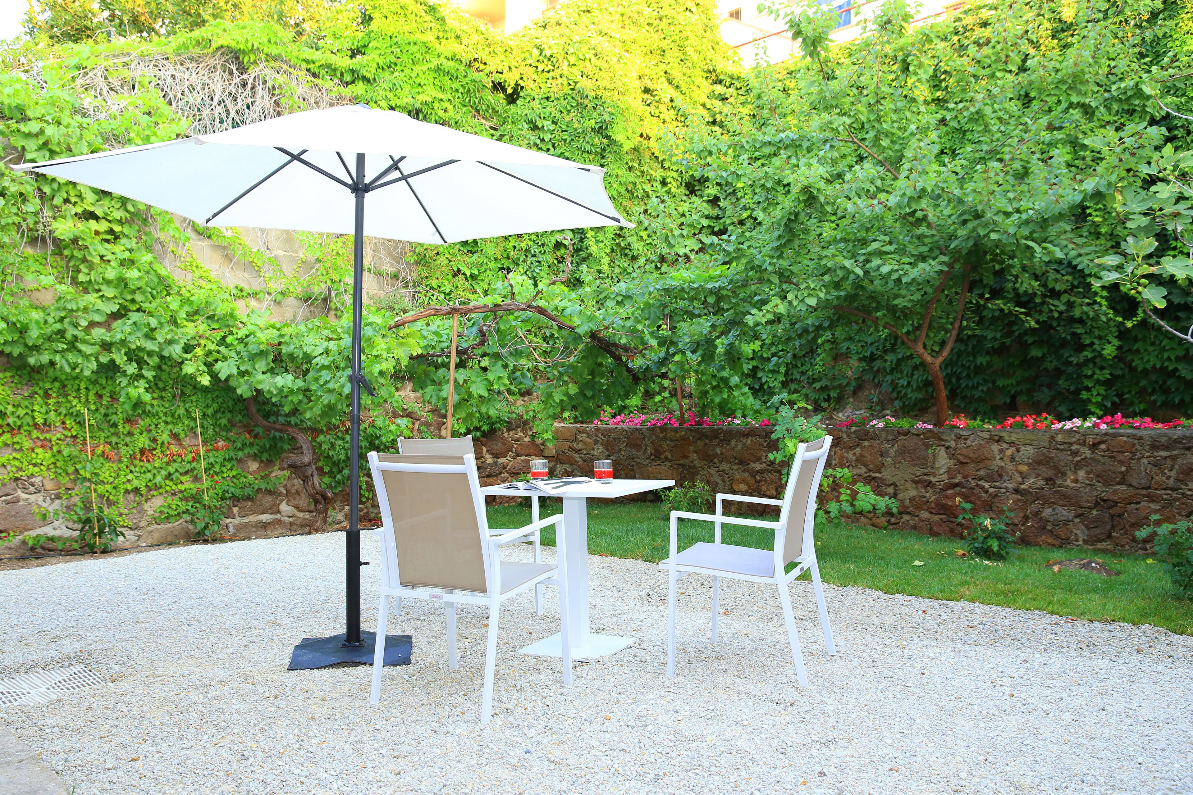 An outdoor patio with a table and two chairs, an umbrella, and a stone wall with greenery.