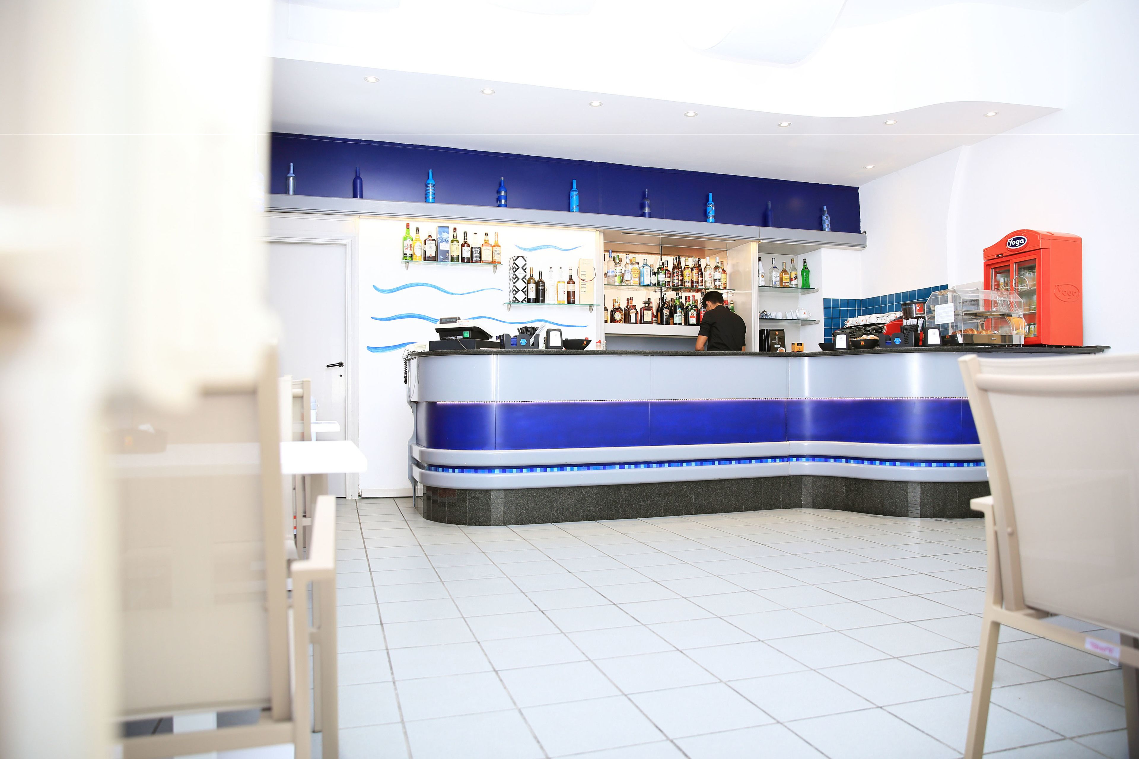 A bar area with a counter, shelves of bottles, and a red machine.