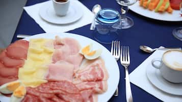 A breakfast setting with a plate of assorted meats, eggs, and cheese, a cup of coffee, and a glass of water on a table.