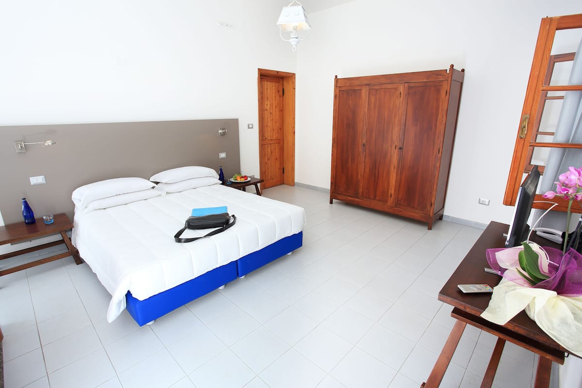 Et soveværelse med seng, natbord, garderobe og et skrivebord med stol.