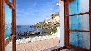 Vista costera desde una ventana con vistas al mar y una colina con edificios.